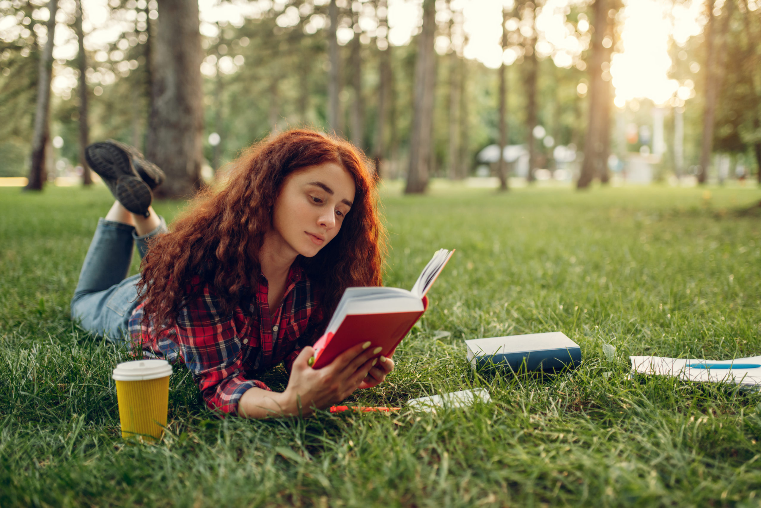 Female student with cup of coffee lying on grass
